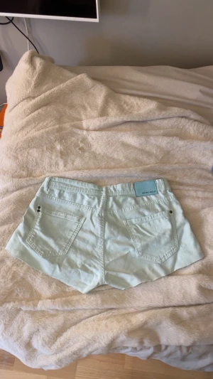 Turkosa denimshorts från Rut&Circle - Snygga turkosa shorts i denim från Rut&Circle. Klassisk femficksmodell med knapp och dragkedja framtill. Shortsen har rå kant nedtill för en avslappnad look och är perfekta för varma dagar.