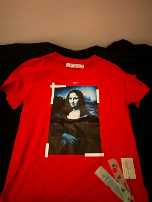 Röd Off-White t-shirt med tryck - Cool röd t-shirt från Off-White med ett stort konstnärligt tryck i blått och svart på framsidan. Klassisk passform och rund hals. Perfekt statement-plagg för dig som gillar streetwear och unika prints.