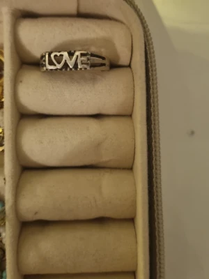 Silverfärgad ring med LOVE-text - Cool ring i silverfärg med texten LOVE där O:et är format som ett hjärta. Ringen har en öppen design med dubbla band på sidorna och är perfekt för att ge din stil en personlig touch.