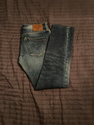Replay smala blå jeans - Snygga blå jeans från Replay med klassisk femficksdesign och smal passform. Jeansen har slitna detaljer och en läderpatch med Replay-logga bak i midjan. Tillverkade i denim med en tvättad look som ger en cool vardagsstil.