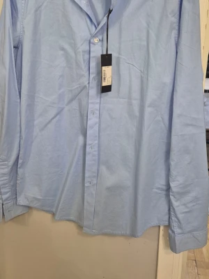 Ljusblå klassisk skjorta S - Snygg ljusblå skjorta med klassisk krage och knappar framtill. Skjortan har lång ärm och är tillverkad i mjuk bomull, perfekt för en clean och stilren look. Passar till både jeans och kostymbyxor.