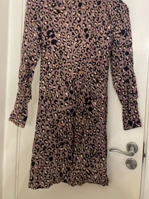 Leopardmönstrad klänning från H&M - Säljer en snygg leopardmönstrad klänning från H&M i storlek 36. Klänningen har långa ärmar, rund halsringning och dragkedja i sidan. Färgen är lila med svarta och beige detaljer. Perfekt för dig som vill sticka ut med ett trendigt mönster.