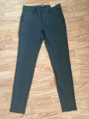 Grå kostymbyxor med smala ränder - Snygga grå kostymbyxor från ONLY & SONS med smala vita kritstrecksränder. Byxorna har slim fit-modell, bälteshällor och sidofickor. Perfekta för en stilren look och passar till skjorta eller t-shirt.