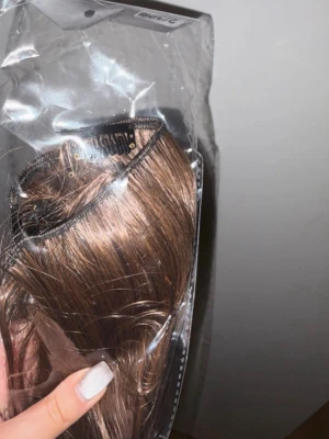 Brun clip-on löshårsslinga 24 inch - Snygg brun clip-on löshårsslinga med lätt vågigt hår. Perfekt för att snabbt få längre och fylligare hår. Fästes enkelt med clips och smälter in naturligt med ditt eget hår. Kommer i förpackning.