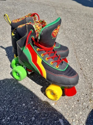 Färgglada Rio Roller rullskridskor - Säljer ett par coola Rio Roller rullskridskor med svart bas och detaljer i rött, gult och grönt. Skorna har röda snören, mönstrad plös och hjul i neonfärger (grönt, gult, rött). Perfekt för dig som vill sticka ut på skatebanan. Materialet är syntet och textil. Storlek 40.