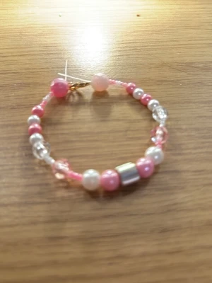 Rosa och vita pärlarmband - Ett handgjort armband med pärlor i rosa, vitt och transparent. Armbandet har en blandning av runda och en fyrkantig metallfärgad pärla, trädd på rosa tråd. Perfekt accessoar för att ge din outfit en söt och lekfull touch.