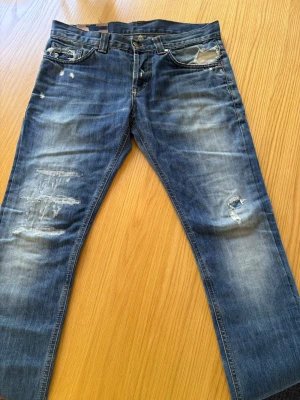 Blå Dondup jeans med slitningar - Säljer ett par blå jeans från Dondup med slitningar. Köpta på plick för typ ett år sedan. Riktigt snygga och sköna men har ett litet hål vid höger bakficka som inte var där från början. Det märks inte jätte mycket vid användning men nämner det ändå. Se mer på bild 3 eller fråga!