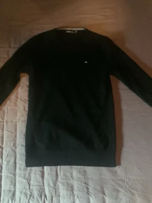 Svart stickad tröja från lidnbergh  - Klassisk svart stickad tröja från j.Lindberg med rund halsringning och diskret logga på bröstet. Tröjan har långa ärmar och ribbade muddar vid ärmslut och nederkant. Perfekt basplagg till garderoben.