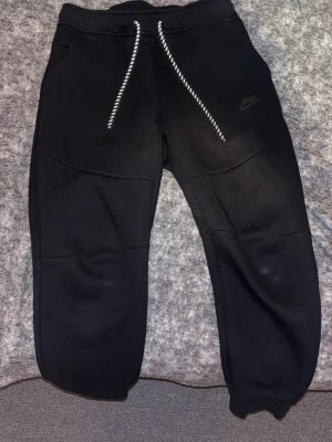 Svarta mjukisbyxor från Nike - Säljer ett par svarta mjukisbyxor från Nike med vita snören och diskret Nike-logga på benet. Byxorna har resår i midjan och vid bensluten samt praktiska fickor. Tillverkade i mjukt och bekvämt material, perfekta för chill dagar.