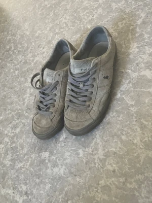 Gråa Polo Ralph Lauren sneakers - Gråa sneakers från Polo Ralph Lauren i mocka med klassisk låg siluett. Skorna har grå snörning, gummisula och den ikoniska Polo-loggan broderad på sidan. Perfekta för en avslappnad och stilren look. Nypris ligger runt 1700kr st:41 men passar 42