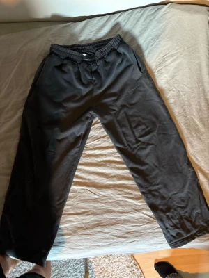 Svarta mjukisbyxor med patchdetaljer - Svarta mjukisbyxor med resår i midjan och sidofickor. Unik design med patchade detaljer längs ena benet som ger en cool och avslappnad look. Perfekta för chill dagar eller streetwear-stil.