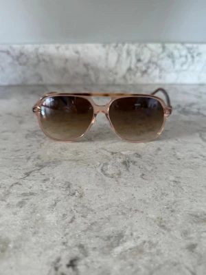 Ray-Ban aviator solglasögon - Snygga solglasögon från Ray-Ban i klassisk aviator-modell med transparent bågar och bruna tonade glas. Skalmarna har sköldpaddsmönster för en extra cool touch. Perfekta för att lyfta din stil under soliga dagar.