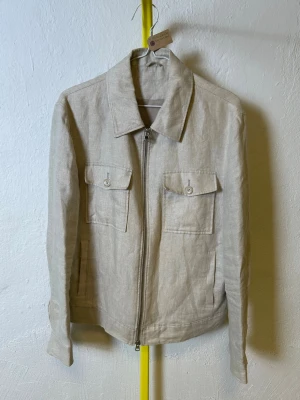 Beige overshirt från These Glory Days  - Denna vara kommer att auktioneras ut på Plick Live den 3 juni klockan 19:00