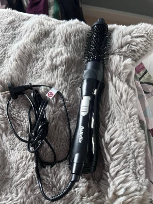 BaByliss svart varmluftsborste - En svart varmluftsborste från BaByliss med rund borste och sladd. Perfekt för att styla och ge volym till håret. Borsten har metallpiggar och handtaget har en silverfärgad knapp för inställningar. Snygg och smidig att använda.