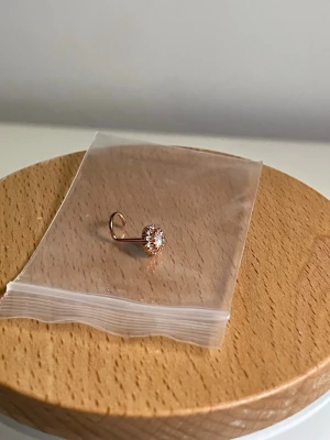 Roséguld 0.8mm piercing surgical steel - Piercing i roséguldfärgat surgical steel med sten i mitten, omgiven av små gnistrande stenar. 0.8mm, och 7mm lång. Oanvänd. Får sanitation rengöring innan den skickas