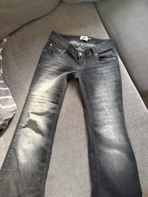 Grå bootcut jeans med slitningar - Säljer ett par grå bootcut jeans med snygga slitningar och tvättade detaljer på låren. Klassisk femficksmodell med knapp och dragkedja. Perfekta för en avslappnad och trendig look. BARA TESTADE