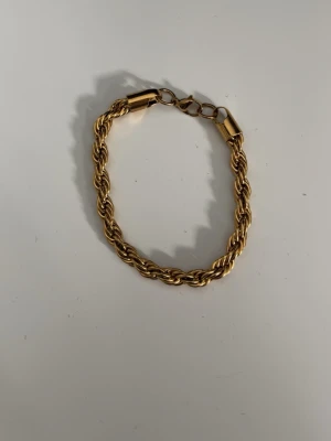 Flätat guldarmband i metall - Snyggt flätat armband i guldfärgad metall med tvinnad design. Perfekt accessoar för att lyfta din stil med en klassisk touch. Armbandet har ett smidigt lås och passar till många olika looks.