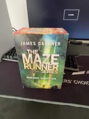 The Maze Runner boxset av Dashner - Säljer en box med The Maze Runner-serien av James Dashner. Boxen har färgstark omslagsdesign i grönt, gult och svart med stora vita och gula bokstäver. Perfekt för dig som gillar spännande dystopiska äventyr och vill ha hela serien samlad.