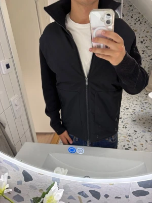 Svart cardigan från massimo Dutti - Snygg svart jacka med hel dragkedja framtill och hög krage. Ärmarna är ribbstickade vilket ger en schysst kontrast till resten av jackan. Perfekt till vardags och enkel att matcha med olika outfits.