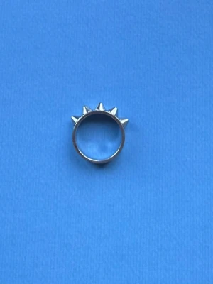 Silvrig ring med nitar - Cool ring i silverfärgad metall med fem spetsiga nitar runt ovansidan. Perfekt accessoar för dig som gillar en edgy och alternativ stil. Ringen har en rund form och är helt i metall.