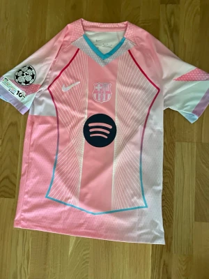 Rosa FC Barcelona matchtröja Nike - Snygg rosa FC Barcelona matchtröja från Nike med vita och ljusblå detaljer. Tröjan har klubbmärke och Nike-logga på bröstet samt Spotify-logga i svart framtill. Tillverkad i lätt och ventilerande syntetmaterial, perfekt för fotboll eller träning. Lamine Yamal