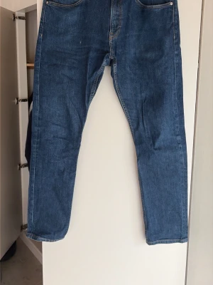 Blå calvin klein x Andy warhol jeans med tryck på bakfickan - Säljer ett par blå calvin klein jeans i rak modell med coolt tryck i rött och vitt på ena bakfickan. Klassisk femficksdesign och normal midja. Jeansen är i denim och har en unik detalj som sticker ut. Perfekta för dig som vill ha något annorlunda i garderoben.