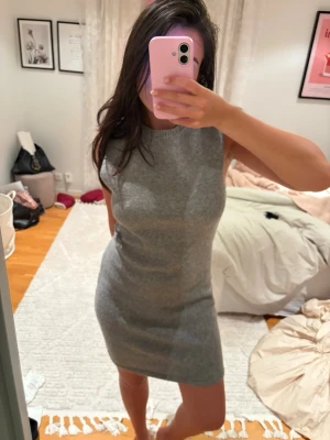 Grå ärmlös stickad klänning - Säljer en enkel och snygg grå stickad klänning i kort modell. Klänningen är ärmlös och har en rund halsringning. Perfekt för dig som gillar en clean och stilren look.