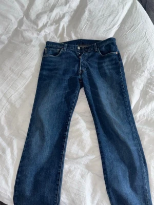Levi's Premium blå jeans 501 Classics - Säljer ett par klassiska blå Levi's Premium jeans med rak passform. Jeansen har fem fickor, knappgylf och är gjorda i slitstark denim av bomull. Perfekta för dig som gillar tidlös stil och vill ha ett par riktigt snygga jeans från ett ikoniskt märke.