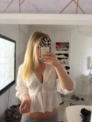Vit blus med spets och v-ringning - Säljer en vit blus med v-ringning och spetsdetaljer. Blusen har långärmade ärmar och knappar framtill. Den är luftig och har en lätt volang nedtill, perfekt för dig som gillar en romantisk och trendig stil.