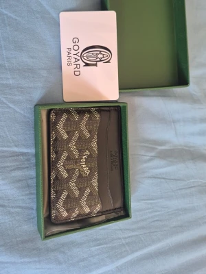 Brun korthållare från G - Snygg brun korthållare från G med klassiskt mönster i beige och vitt. Tillverkad i läder med flera fack för kort. Kommer i originalask och med G -kort. Perfekt accessoar för dig som gillar exklusiva detaljer.