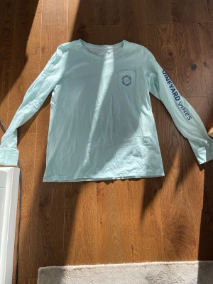 Ljusblå långärmad t-shirt Vineyard Vines - Ljusblå långärmad t-shirt från Vineyard Vines med tryck på bröstet, ryggen och längs ena ärmen. Skön passform och klassisk rund halsringning.