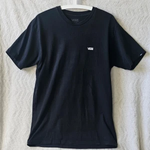 Svart t-shirt från Vans i bomull - Klassisk svart t-shirt från Vans med liten vit logga på bröstet. T-shirten har rund halsringning och är tillverkad i mjuk bomull. Perfekt för en avslappnad och stilren look.