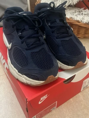Nike V5 RNR  - Snygga mörkblå Nike sneakers med vit sula och vit swoosh på sidan. Ovandelen är i mesh och syntetmaterial för bra andningsförmåga. Skorna har svarta skosnören och detaljer i gummi på sulan. Perfekta för en sportig och trendig look.