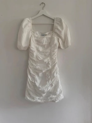 Vit kort klänning med puffärm från NAKD - Trendig vit kort klänning med puffärmar från NAKD. Klänningen har en smickrande, åtsittande passform och kan bäras offshoulder för en cool look. Sparsamt använd. Perfekt för student, midsommar mm