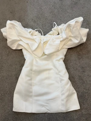 Fashion Nova vit volangklänning studentklänning - Superfin vit kort klänning med stora volangdetaljer över axlarna och smala axelband. Klänningen har en figurnära passform och är perfekt för dig som vill sticka ut. Materialet känns slätt och har en lätt glans.