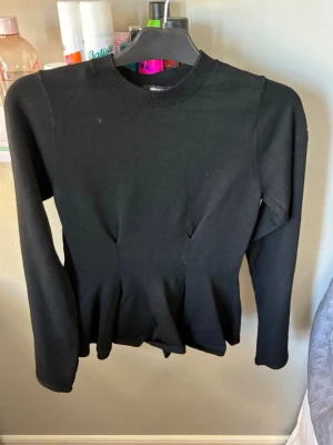 Svart långärmad topp från Gina Tricot - Snygg svart långärmad topp från Gina Tricot med rund halsringning och figurnära passform. Toppen har en lätt utsvängd nederdel som ger en peplum-effekt. Perfekt att styla med jeans eller kjol. Nypris 300+