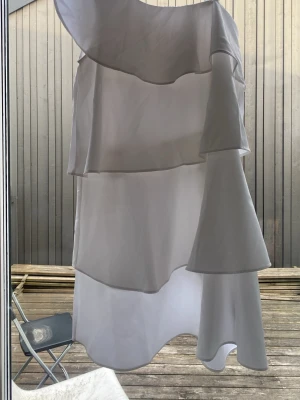Vit oneshoulder volangklänning - Superfin vit klänning med oneshoulder och flera lager volanger. Klänningen har asymmetrisk design och är perfekt för dig som vill sticka ut. Lätt och luftig känsla, passar till sommarens alla tillfällen. Den har en liten smink fläck vid toppen