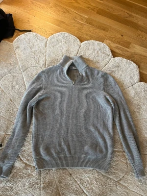 Grå stickad tröja med dragkedja Zara - Snygg grå stickad tröja från Zara med halv dragkedja i halsen och ribbstickad struktur. Perfekt för lager-på-lager och enkel att matcha med jeans eller chinos. Tröjan har långa ärmar och hög krage för extra stilpoäng.