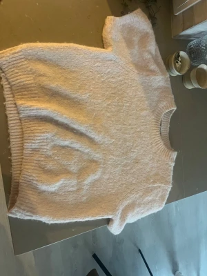 Ljusbeige/rosa stickad kortärmad tröja - Mysig ljusbeige stickad tröja med korta ärmar och rund hals. Tröjan har en fluffig och mjuk känsla. Från Gina tricot