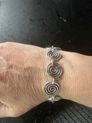 Silverfärgat armband med spiralform - Snyggt armband i silverfärgad metall med flera spiralformade länkar som ger en cool och modern look. Armbandet har ett magnetlås och passar perfekt för dig som gillar unika detaljer. Spiralerna är platta och blanka vilket gör att armbandet sticker ut.