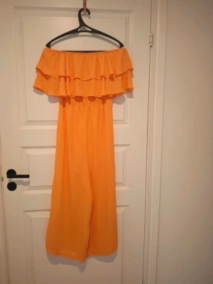 Orange off shoulder jumpsuit Bik Bok - Orange jumpsuit från Bik Bok. Off shoulder-modell med volang upptill. Vida ben och resår i midjan. Tunn och luftig i materialet.