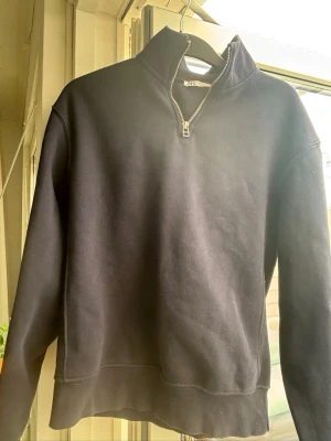 Mörkblå halfzip hoodie från Zara - Mörkblå hoodie från Zara med halv dragkedja och hög krage. Tillverkad i mjukt material som känns skönt mot huden. Perfekt för en avslappnad och stilren look. Klassisk passform och ribbade muddar vid ärmslut och nederkant.