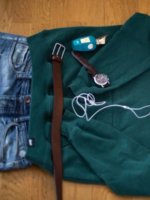 Mörkgrön hoodie med tryck - Mörkgrön hoodie från Sthlm United med vitt rundtryck på bröstet. Klassisk modell med huva och dragsko samt stor magficka framtill. Perfekt för en avslappnad och cool stil. Mjuk bomullsblandning som känns skön mot huden.