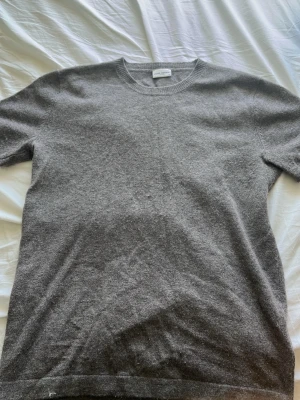 Grå t-shirt i merinoull från John Henric  - En stilren grå t-shirt från John Henric i mjuk merino ull. Klassisk rund halsringning och korta ärmar. Perfekt för dig som gillar minimalistisk och clean stil. Sitter perfekt till sommaren