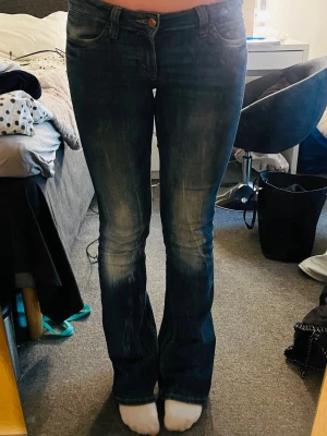 Bootcut jeans i mörkblå denim - Snygga bootcut jeans i mörkblå denim med lätt slitning och klassisk femficksmodell. Jeansen har låg midja och utsvängda ben, perfekta för en trendig och avslappnad look. Stängs med knapp och dragkedja framtill.               Stl 29/34