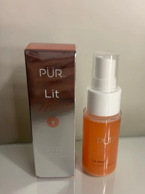 PÜR Lit Mist Face Mist - PÜR Lit Mist är en ansiktsspray i en genomskinlig plastflaska med vit spraypump. Innehållet är orangefärgat och ger en uppfriskande känsla. Kommer i en snygg förpackning med metallicfinish. Perfekt för att ge huden lyster och fixera makeup. Det är som en settingspray tror jag, den är aldrig använd inte ens öppnad.