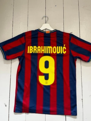 Barcelona Ibrahimović fotbolls tröja - Säljer en klassisk FC Barcelona matchtröja med röda och blå vertikala ränder, gult Nike-märke och Unicef-logga på bröstet. På ryggen står Ibrahimović och nummer 9 i gult. Tröjan är i lätt och ventilerande material, perfekt för sommarvärmen eller träningar.