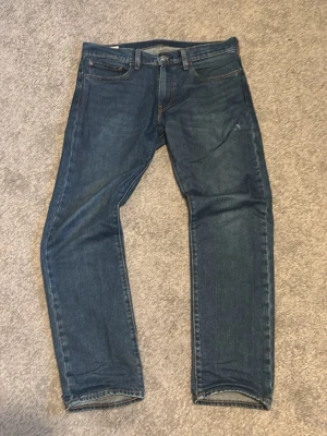 Jeans från Levi's - Klassiska blå jeans från Levi's med rak passform och fem fickor. Jeansen har en mörk tvätt och är tillverkade i slitstark denim. Perfekta för en avslappnad och tidlös stil. Modell: 502