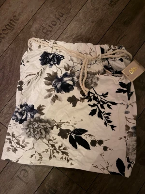 Vit blommig byxa med snörning Cecil - Mjuk och luftig byxa från Cecil i vit färg med stora blommiga mönster i svart och grått. Byxan har snörning i midjan och avslappnad passform, perfekt för chill dagar hemma.