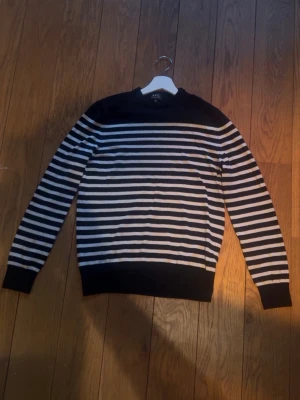Randig stickad tröja från A.P.C. - Snygg stickad tröja från A.P.C. med klassiskt svartvitt randigt mönster. Tröjan har rund halsringning, långa ärmar och ribbade muddar vid ärmslut och nederkant. Perfekt för en stilren och avslappnad look.